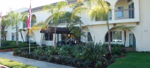 Two-story senior living building with arches, palm trees, and a landscaped entryway
