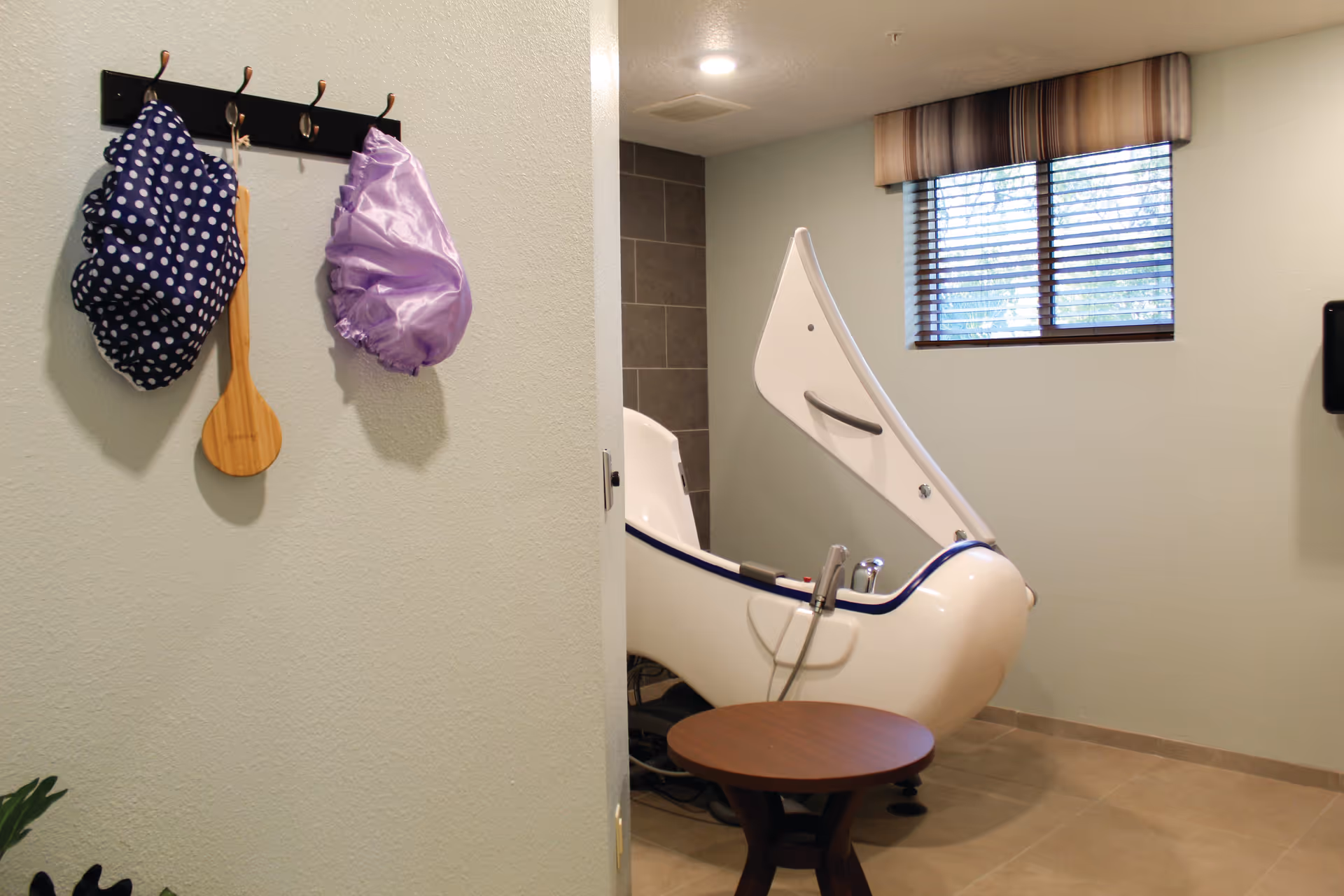 In a memory care facility bathroom, an accessible hydrotherapy tub sits beside a round wooden table.