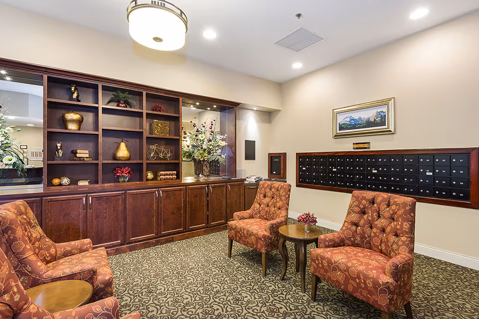 A warm interior lounge with patterned armchairs, a small round table, wooden built-in shelving and a wall of mailboxes.