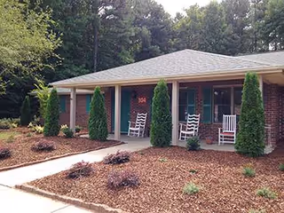 Exterior view of a brick senior living facility front with rocking chairs on the porch.