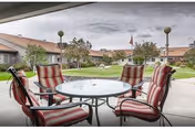 Round outdoor table surrounded by striped cushioned chairs on a covered patio overlooking a landscaped courtyard and surrounding buildings.