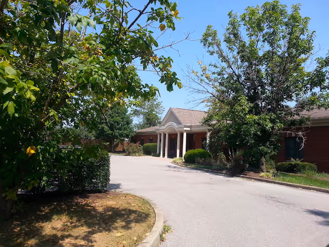 Exterior view of The Breckinridge Memory Care facility with driveway and trees.