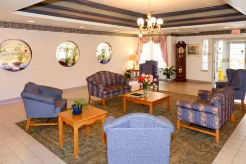 Interior lounge in a senior facility with blue seating, round windows, and a chandelier.