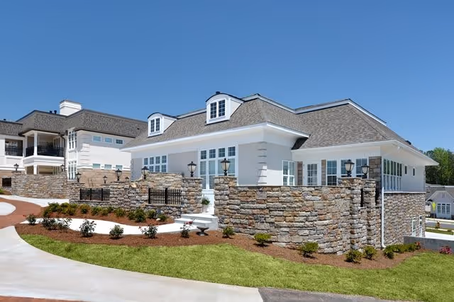 Exterior view of a white multi-level building with stone retaining walls, lanterns, landscaping, and a clear blue sky.