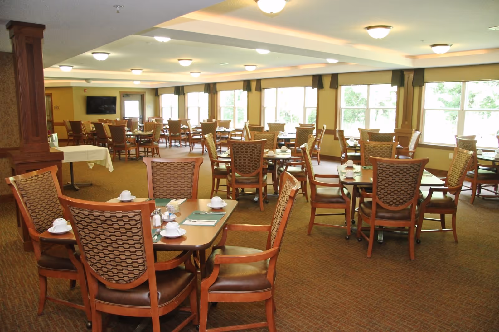 Spacious dining room with multiple set tables and wooden chairs arranged near large windows.