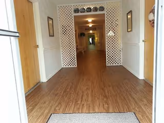 Entrance view of a long interior hallway with wood-look flooring, a lattice archway and doors on both sides.