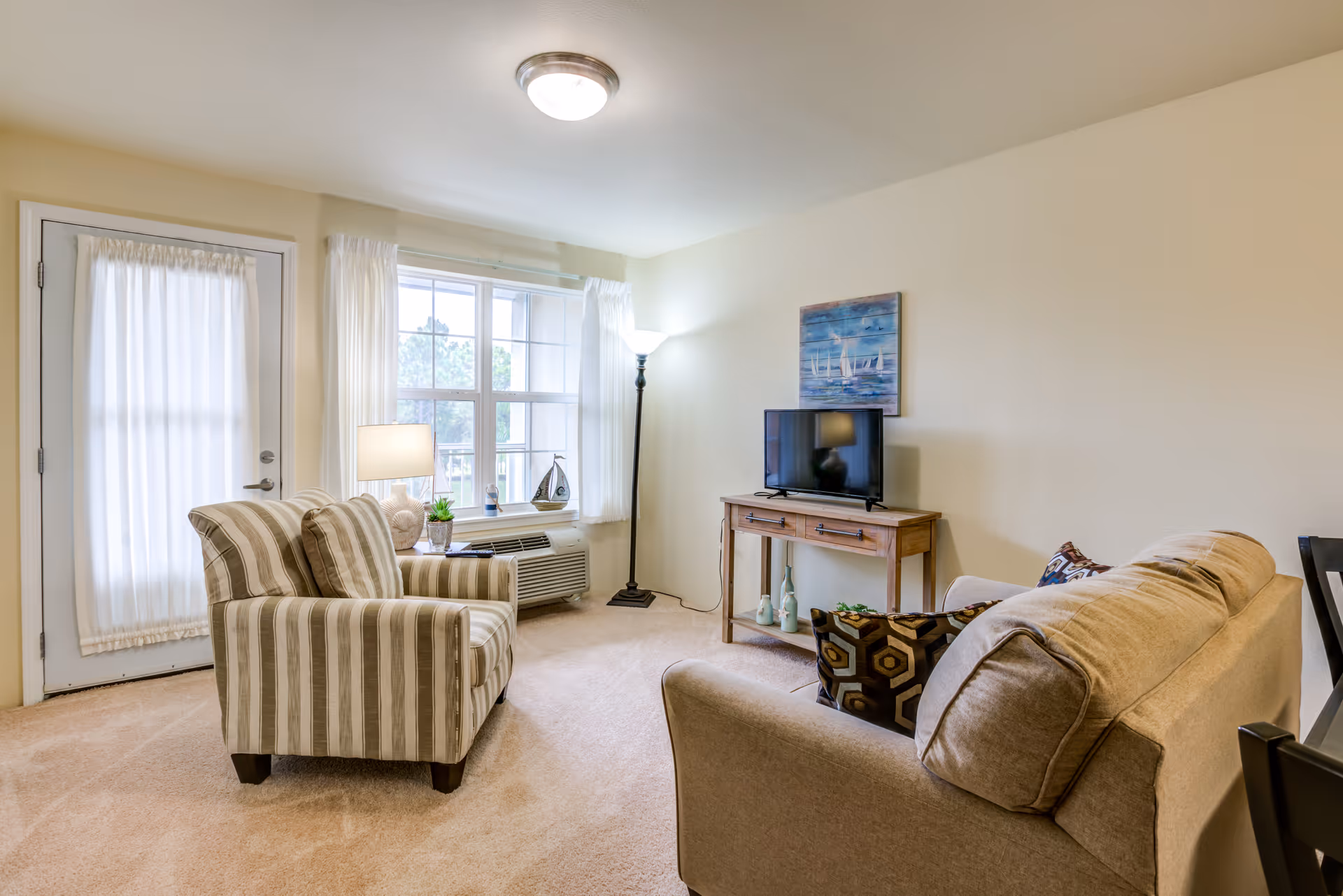 Bright living room with a striped armchair, sofa, TV on a wooden console, and a windowed door.