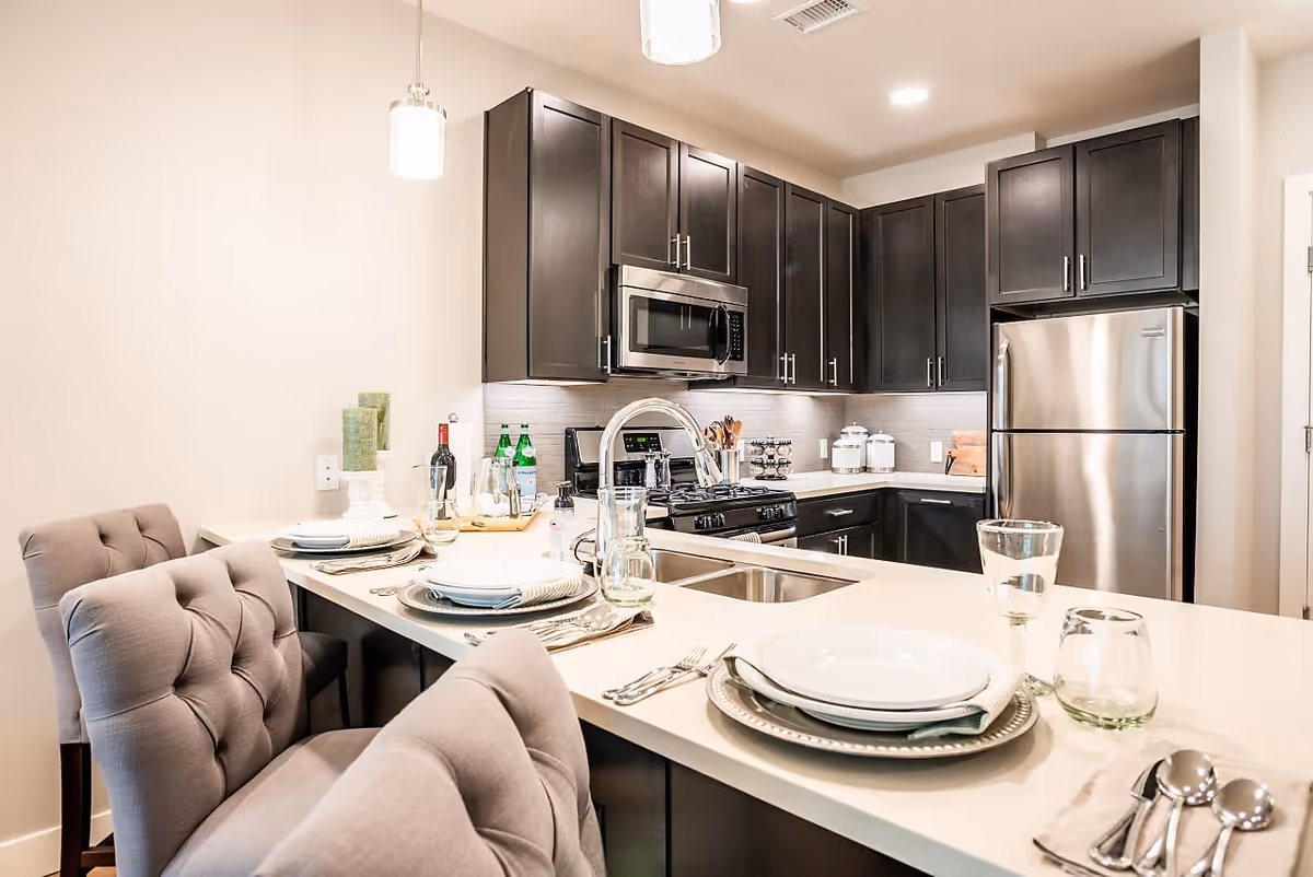 Modern kitchen with dark cabinets, stainless steel appliances and a set dining island with tufted bar chairs.