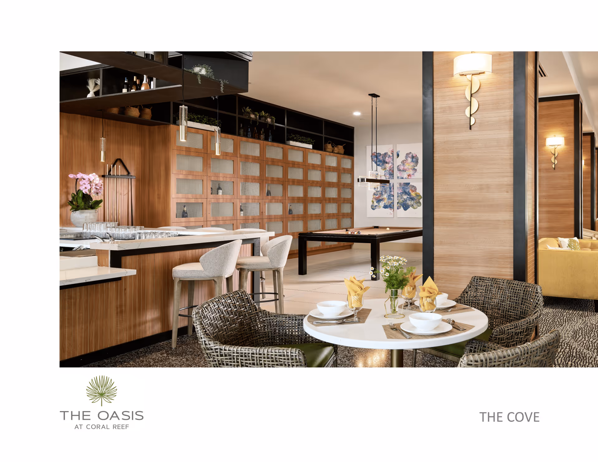 A modern communal lounge with a round dining table set for four, a bar with stools, and a pool table in the background.