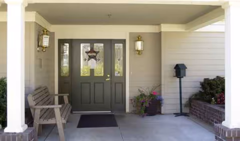 Entrance porch of Farmington Square Tualatin, featuring a dark door, bench, lanterns, and plants.