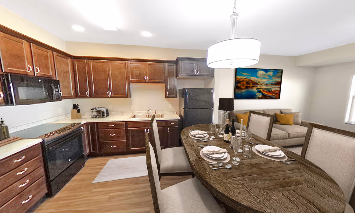 A combined kitchen and dining area featuring dark wood cabinets, a black refrigerator, stove, and microwave. The dining table is set with plates, glasses, and silverware, and there is a modern light fixture hanging above it. In the background, there is a beige couch with yellow and beige cushions and a colorful painting on the wall.