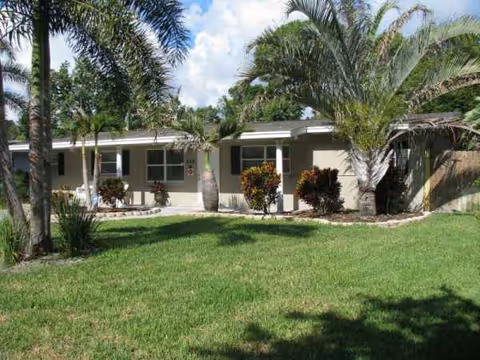 Front exterior of a single-story assisted living facility with palm trees and a green lawn.