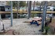 Gravel backyard with a picnic table and trees overlooking a narrow canal with boathouses across the water.