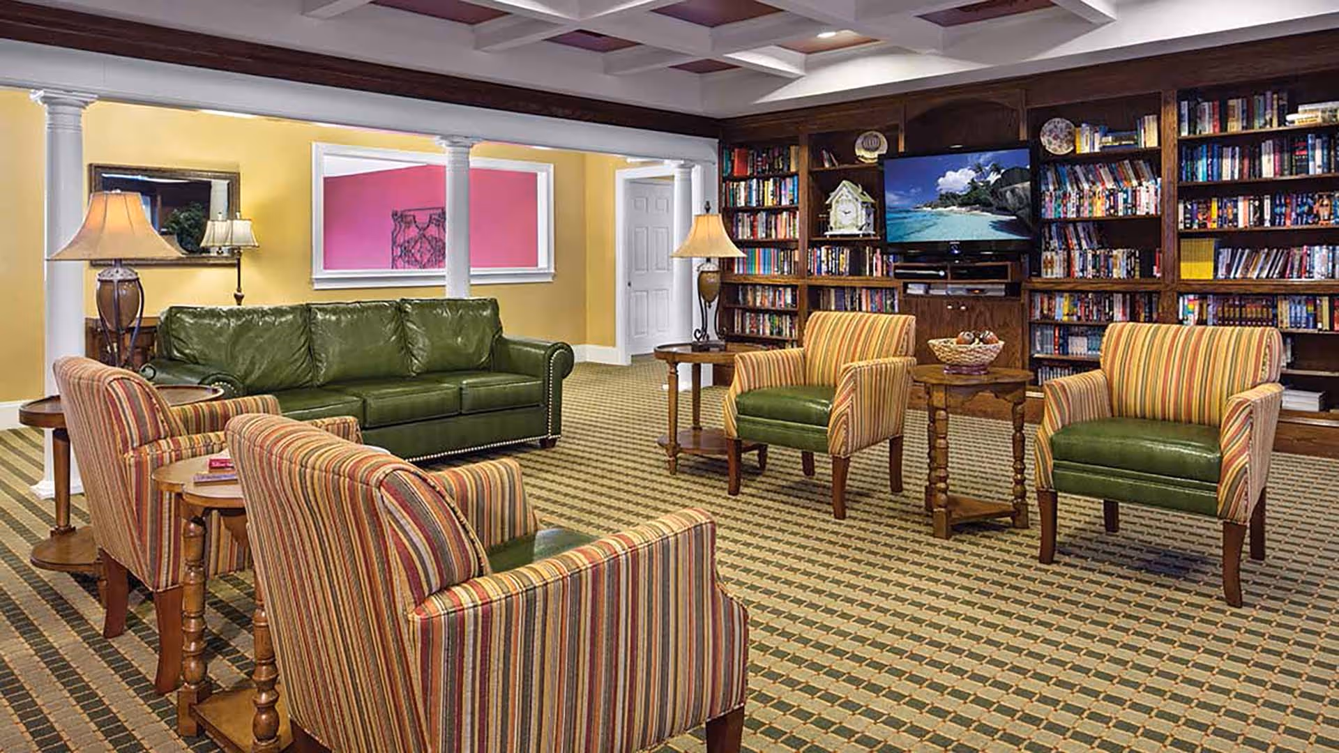 Cozy lounge with striped armchairs, a green leather sofa, side tables and lamps, and built-in bookshelves with a TV.