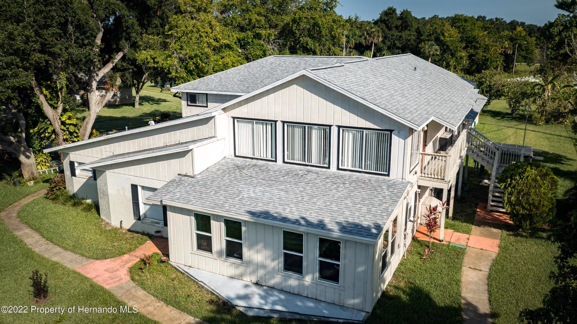Aerial view of a two-story white building with multiple windows, walkways and surrounding lawns and trees.