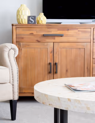 Wooden media cabinet with decorative vases and a TV, beside an upholstered armchair and a round mosaic coffee table with magazines.