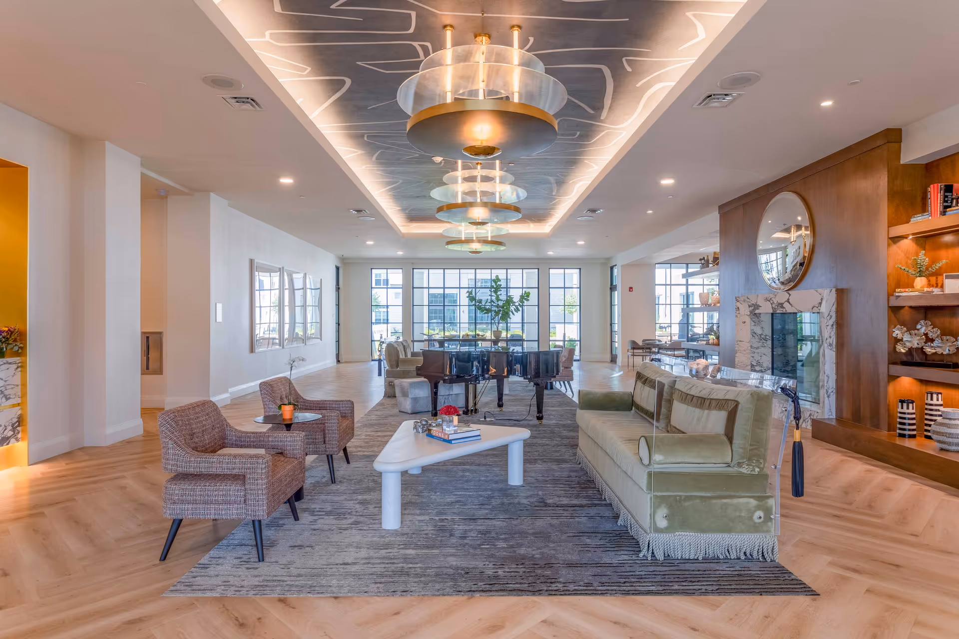 A modern lobby at Opus East Memphis featuring stylish seating, a grand piano, and large windows allowing natural light to fill the space. The ceiling is adorned with contemporary light fixtures, and a cozy atmosphere is created with warm colors and elegant decor.