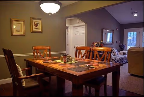 A wooden dining table with chairs in a warmly lit senior living dining room.