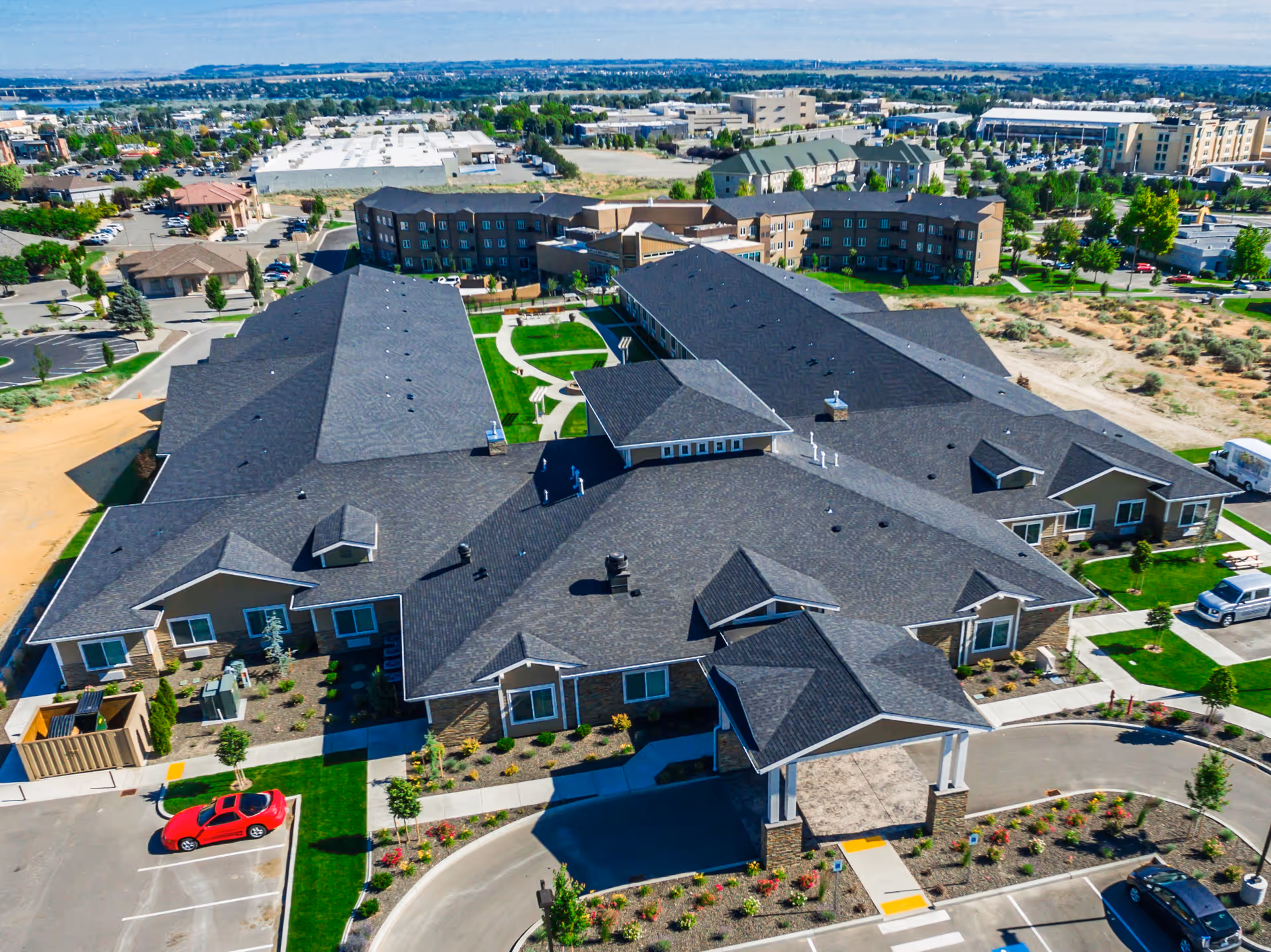 Aerial view of a memory care facility complex with dark shingled roofs, landscaped courtyards, driveways, and parking.