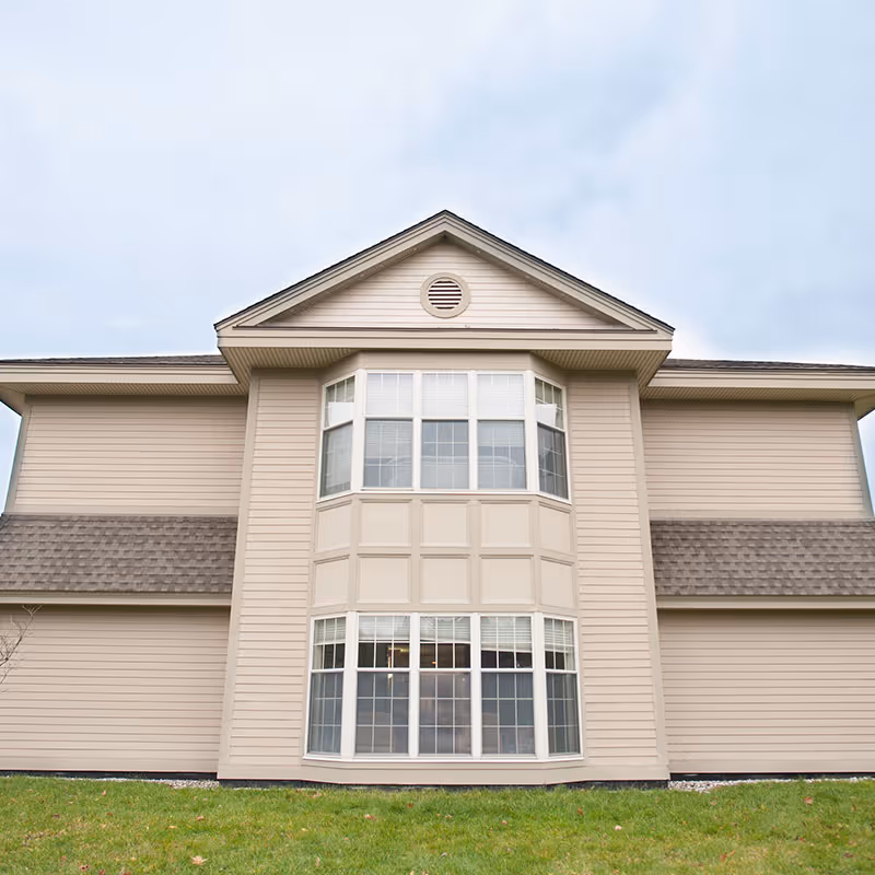 Beige two-story building front with a central three-section bay window and a grassy lawn in front.
