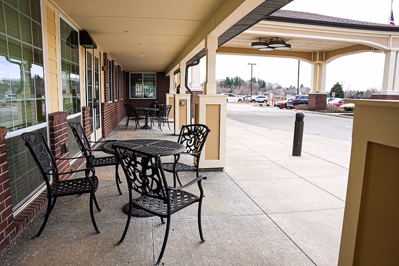 Covered front entrance patio with decorative metal tables and chairs and a drive-up drop-off area.