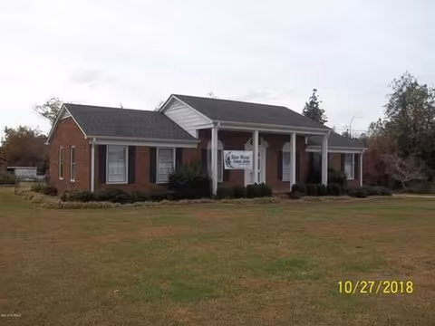 Front exterior of a brick senior living facility with a lawn and entry porch.