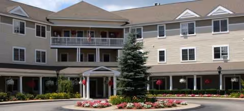Exterior view of Traditions of Dedham building with entrance, balconies, and landscaped circular driveway.