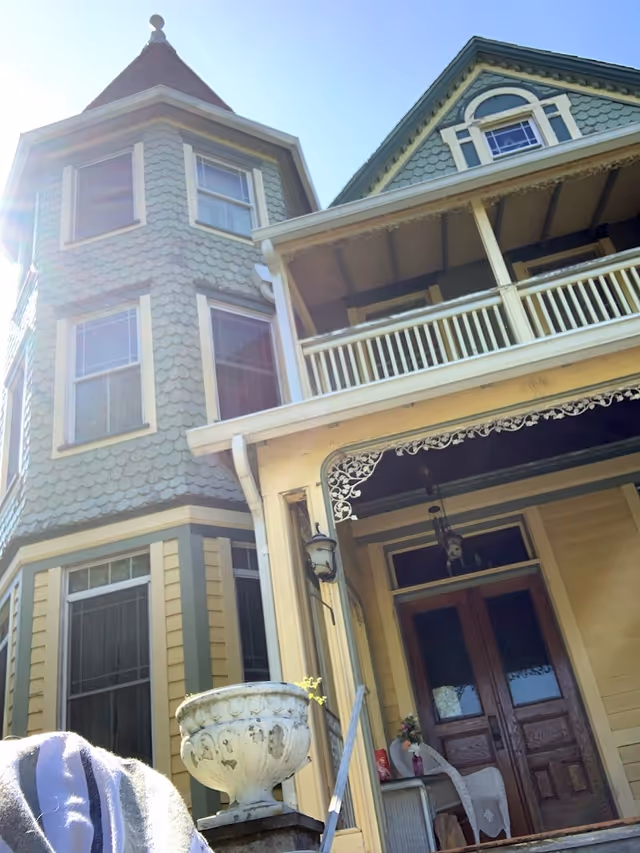 Front exterior of a Victorian-style house with a turret, covered porch, decorative trim, and double wooden entry doors.
