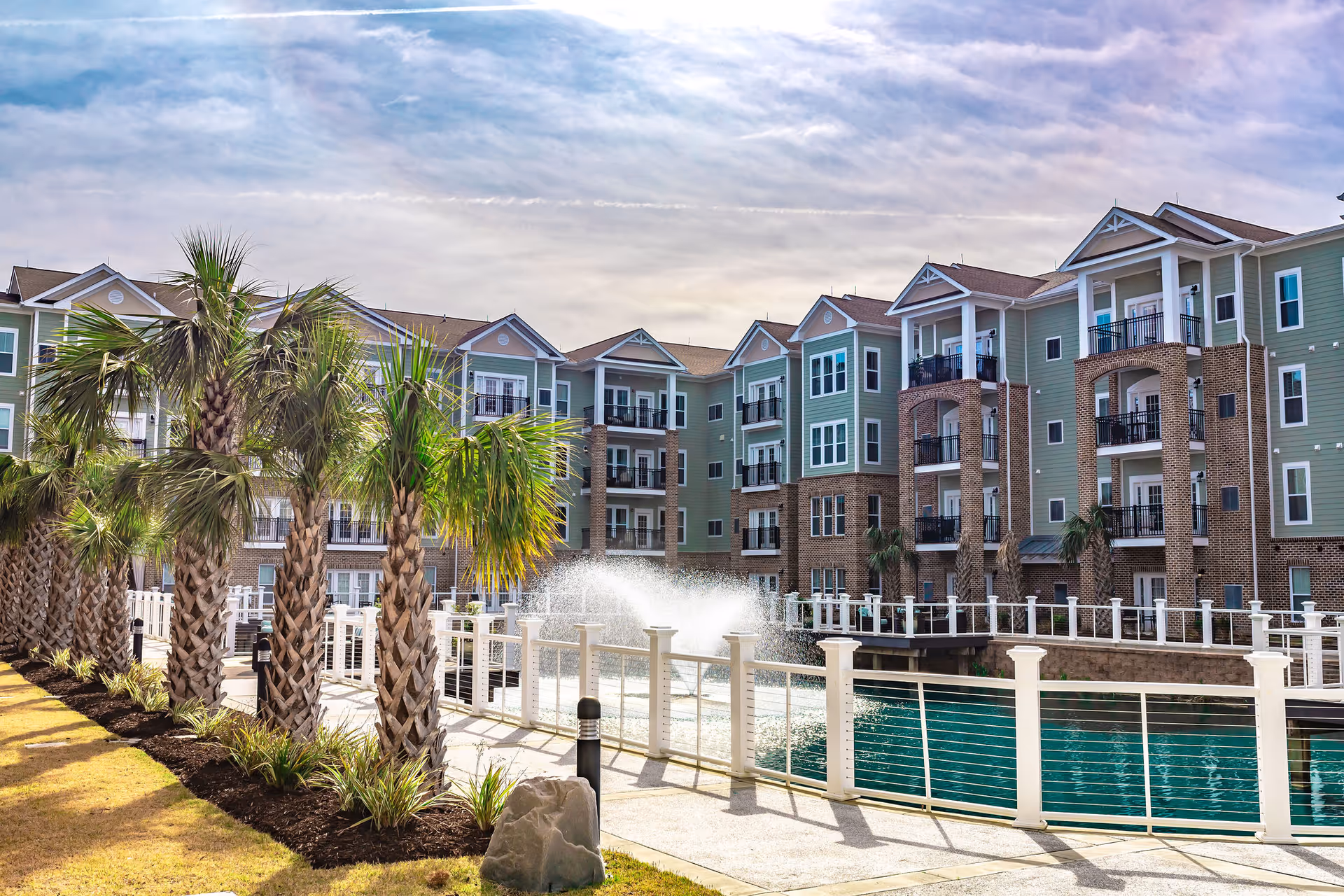 Colorful multi-story senior living building with balconies overlooking a water feature and palm trees.