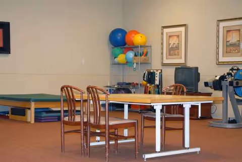 Interior rehabilitation room with a table, chairs, mats, and exercise equipment.