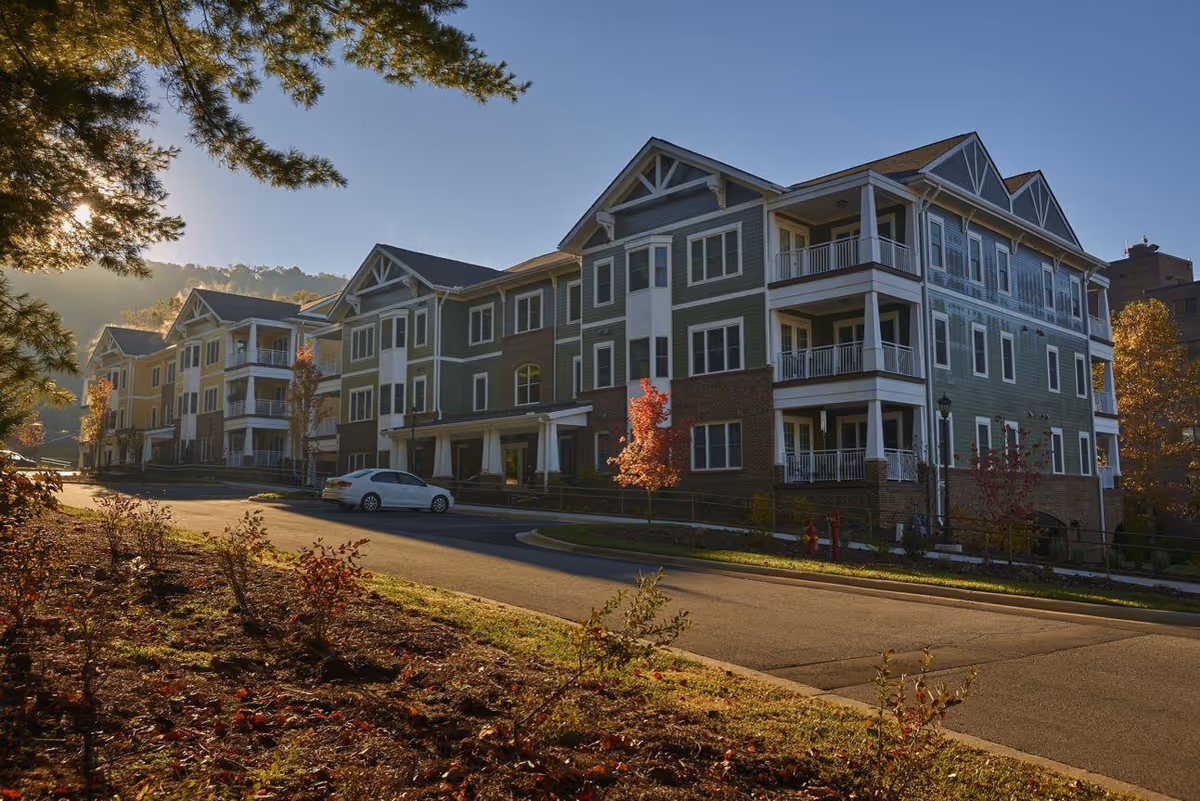 Multi-story residential building with balconies and a driveway in front lit by low sunlight.