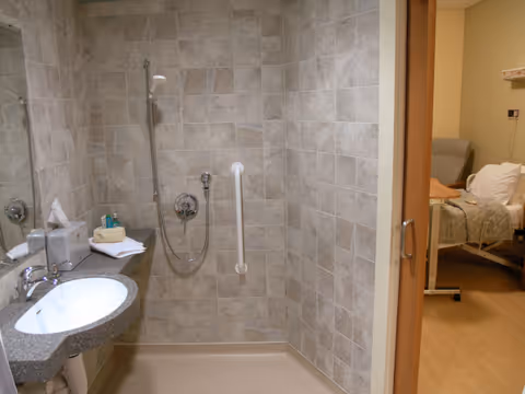 Accessible bathroom with sink, grab bars, shower, and doorway to a bedroom.