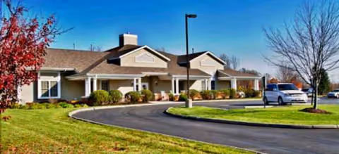 Vista Veranda senior living exterior with curved driveway, manicured lawn, and a parked van.