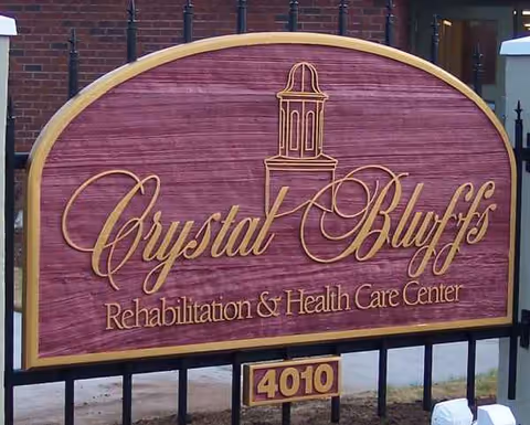 Maroon wooden sign for Crystal Bluffs Rehabilitation & Health Care Center, displaying 4010