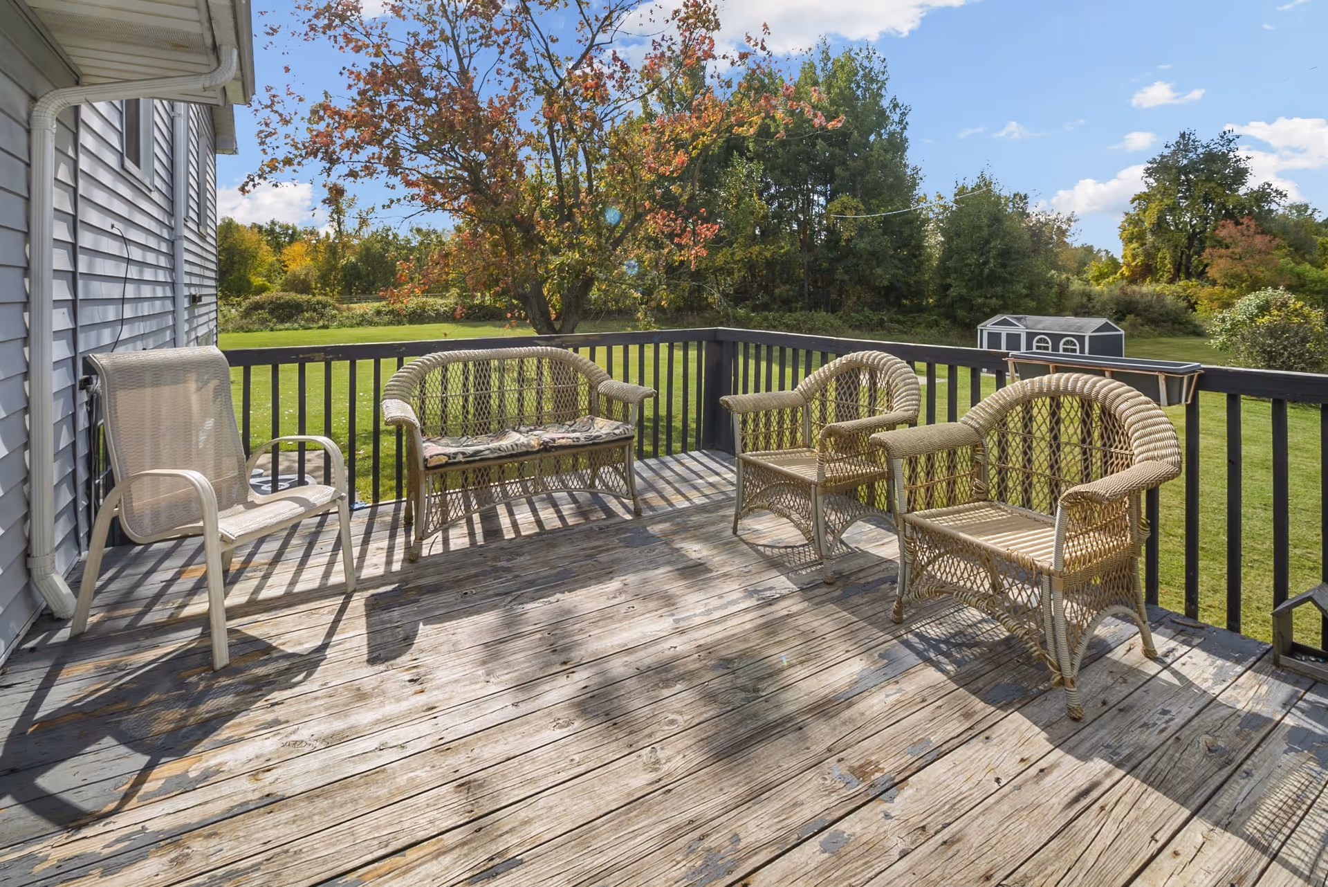 Wooden deck with wicker chairs and a bench overlooking a grassy yard and trees.