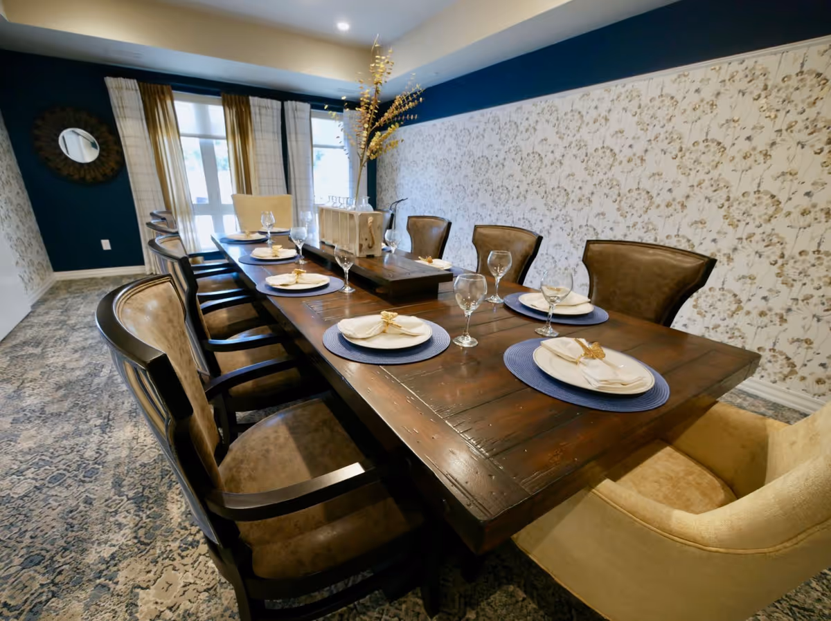 Long wooden dining table set with plates, napkins, and wine glasses surrounded by upholstered chairs in a decorated dining room.