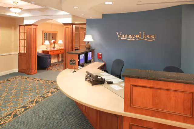 Reception desk and lobby area with a curved front desk, seating, and a blue wall sign reading 'Vantage House'.