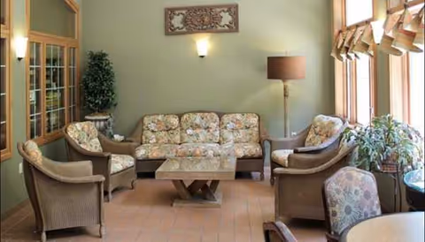 Cozy common living room with floral couches, chairs, plants, and a glass coffee table.