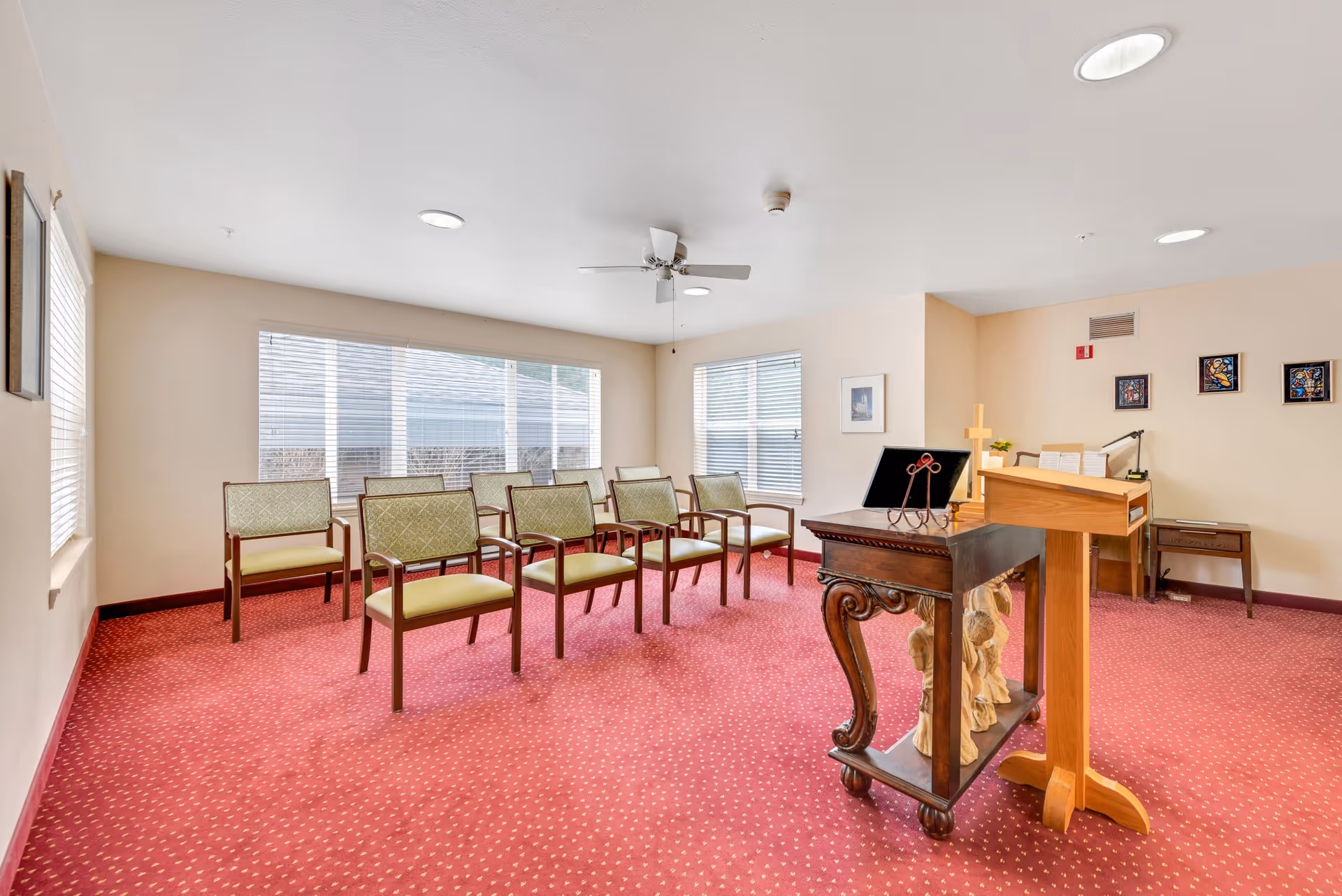 Small chapel-style meeting room with rows of chairs, a lectern and a decorative table on red carpet.