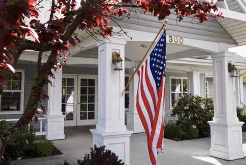 White columned porch of Trustwell Living at Suncrest Place with an American flag.