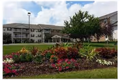 Exterior view of Rosewood Villas senior housing with manicured lawn and colorful garden in foreground.