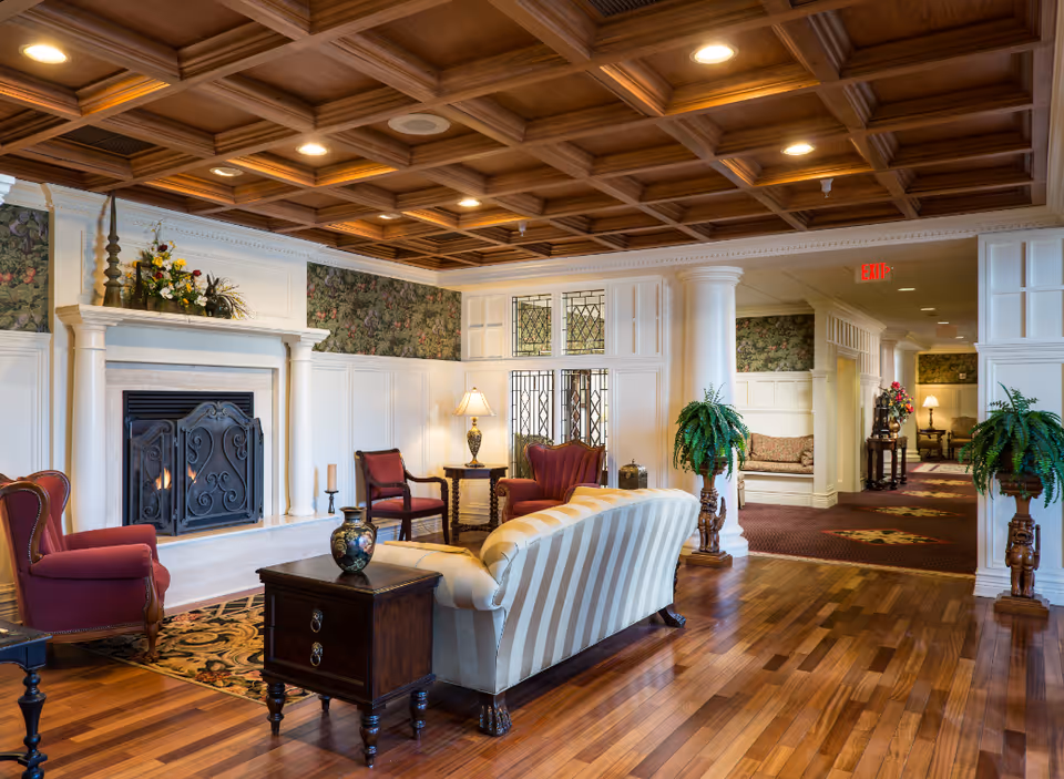 Elegant lounge area with a fireplace, upholstered chairs and a striped sofa beneath a coffered wood ceiling.