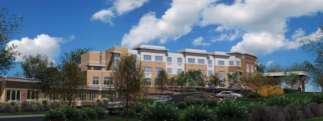 Front exterior view of a multi-story senior living facility with landscaped grounds and parked cars under a blue sky.