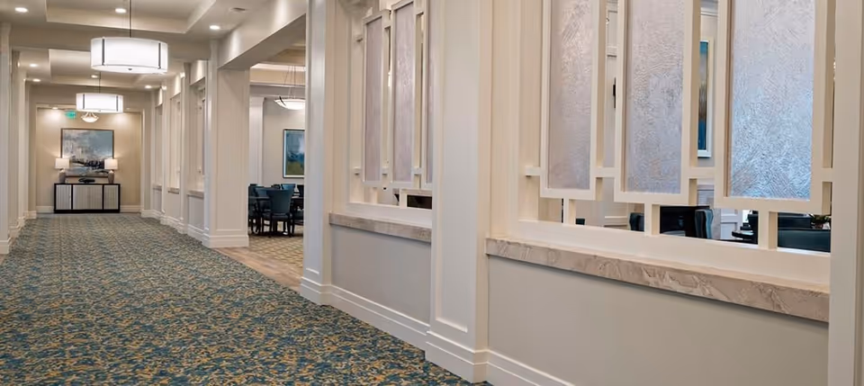 Well-lit carpeted interior corridor with decorative wall panels and a seating/dining area visible through openings.
