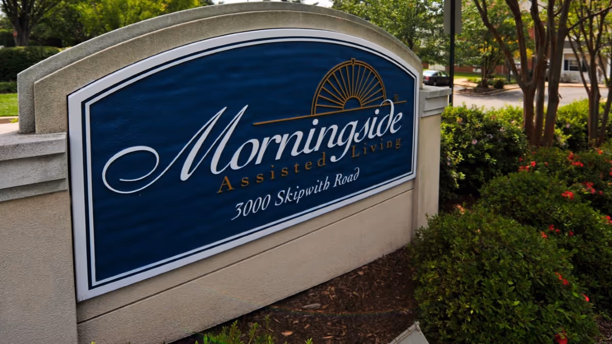 A blue entrance sign for Morningside Assisted Living at 3000 Skipwith Road set among landscaped shrubs.