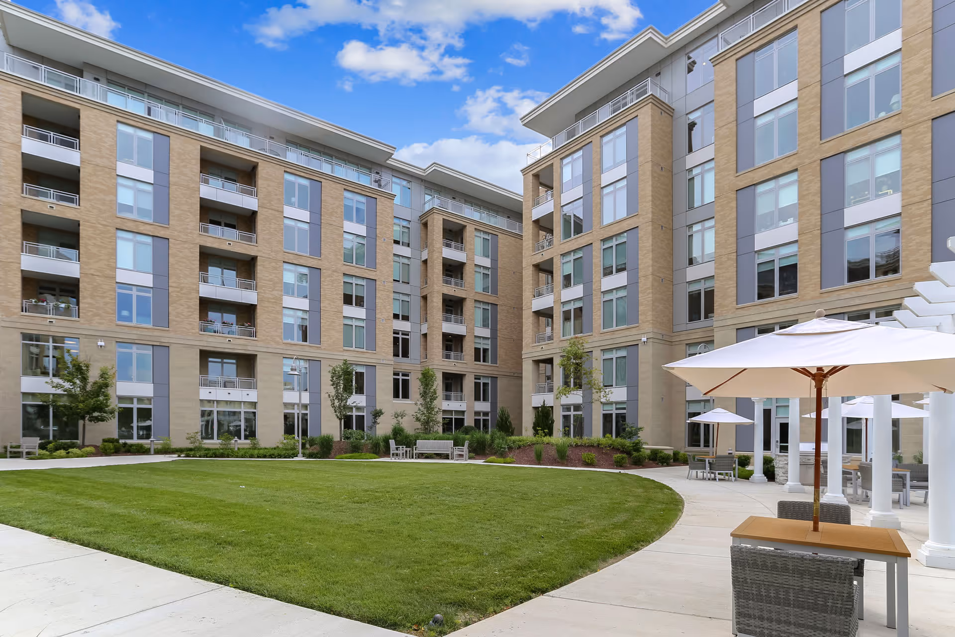 Courtyard of a multi-story senior living building with a grassy lawn, patio umbrellas, and surrounding balconies.