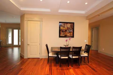 A wooden dining table with six chairs in a warm beige, softly lit room.