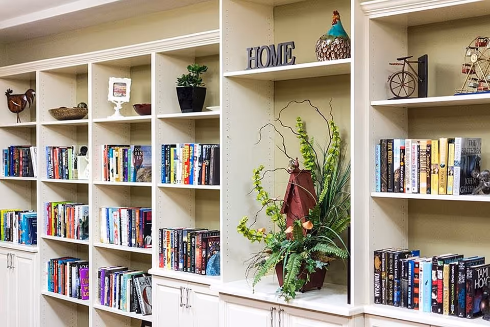 A well-organized bookshelf filled with various books and decorative items including a potted plant, a rooster figurine, a small bicycle model, a Ferris wheel model, and a decorative sign spelling 'HOME'.