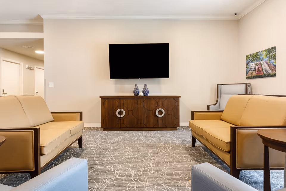 Well-lit lounge with two beige sofas facing a wall-mounted TV above a wooden console in a comfortable sitting area.