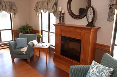 Cozy living room with a wooden fireplace, seating, and large windows.